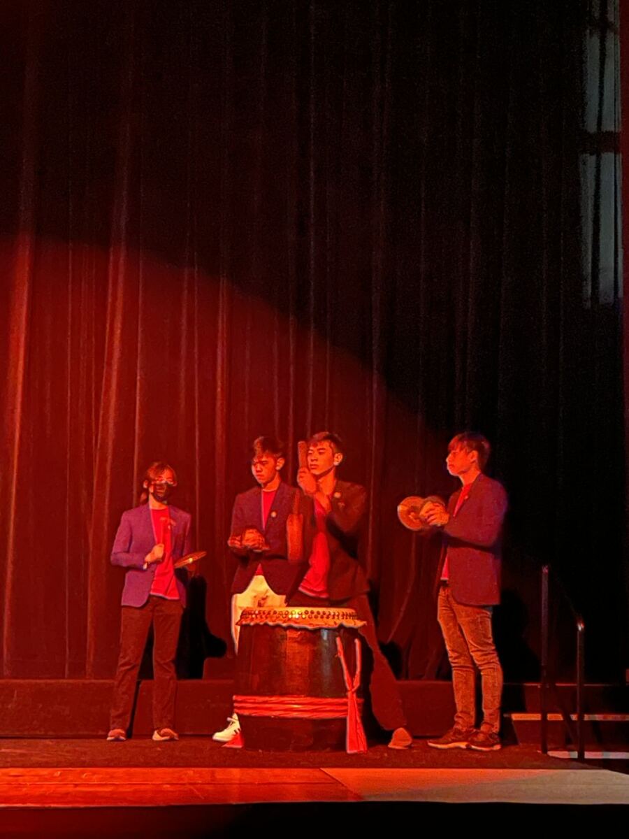 Four performers playing the drum and cymbals on stage under red lights
